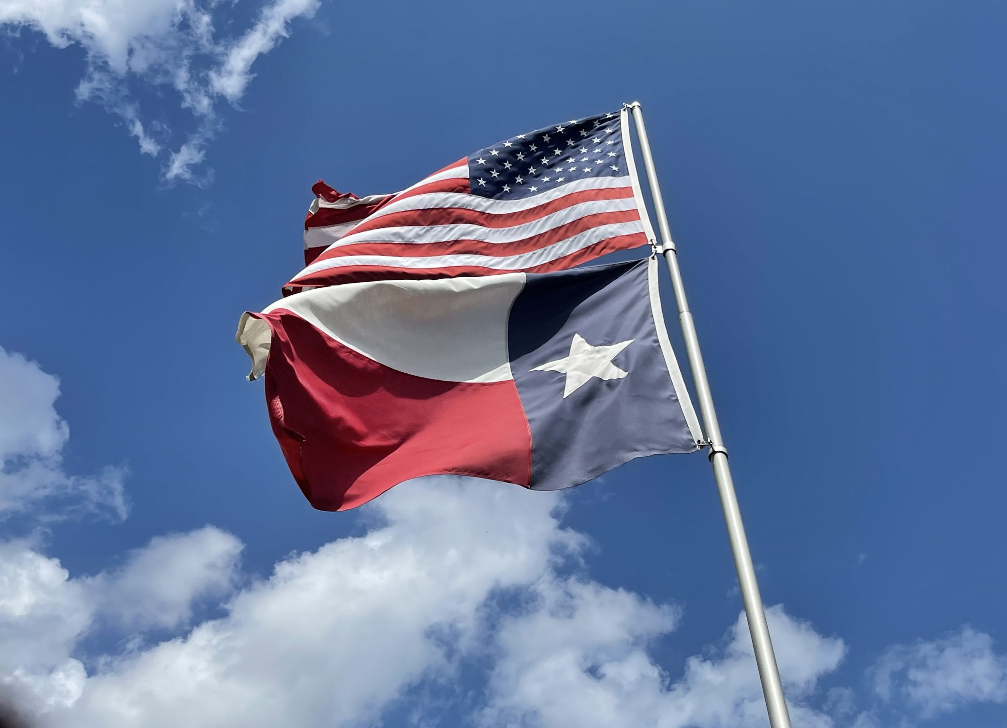 Texas and American flags flying against a blue sky in northwest Houston